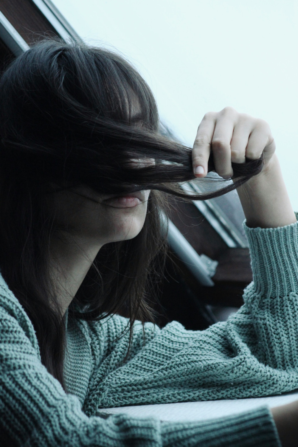 Девушка сидит возле окна и трогает волосы, тревожность, креативность